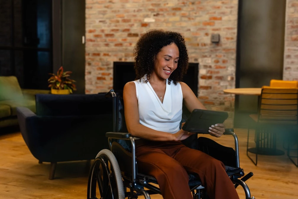 Woman sitting in living room in wheelchair looking at tablet