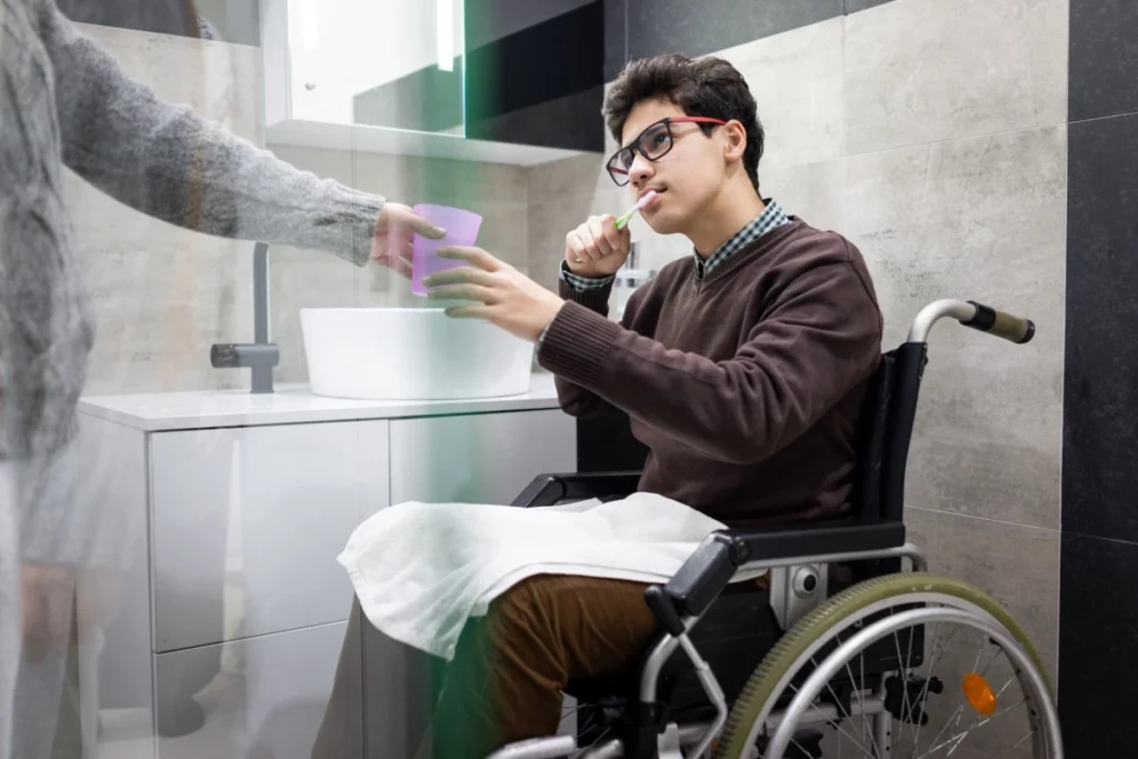 Disabled man in wheelchair brushing teeth with help of support worker