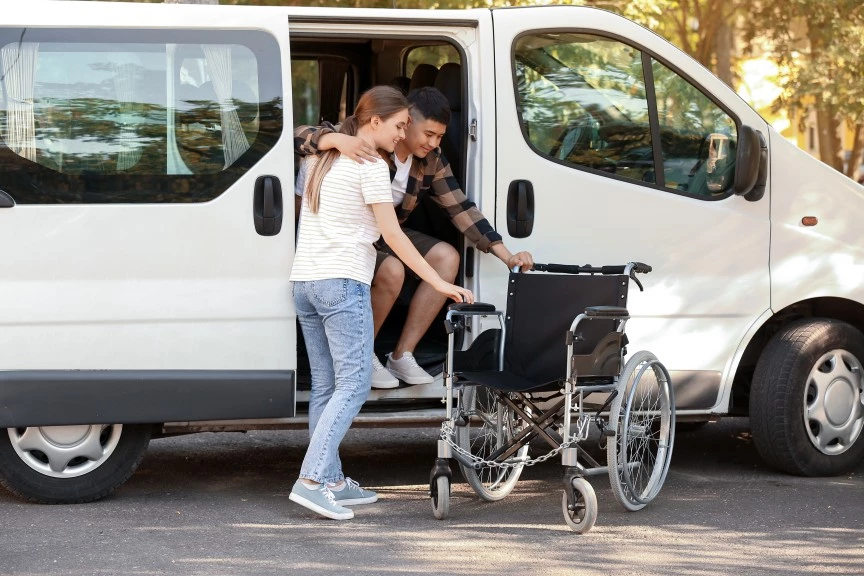 Support worker helping man in wheelchair get out of van