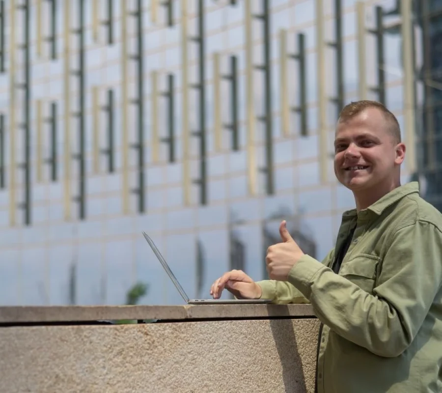 Disabled man on laptop outside while smiling at camera and putting thumbs up